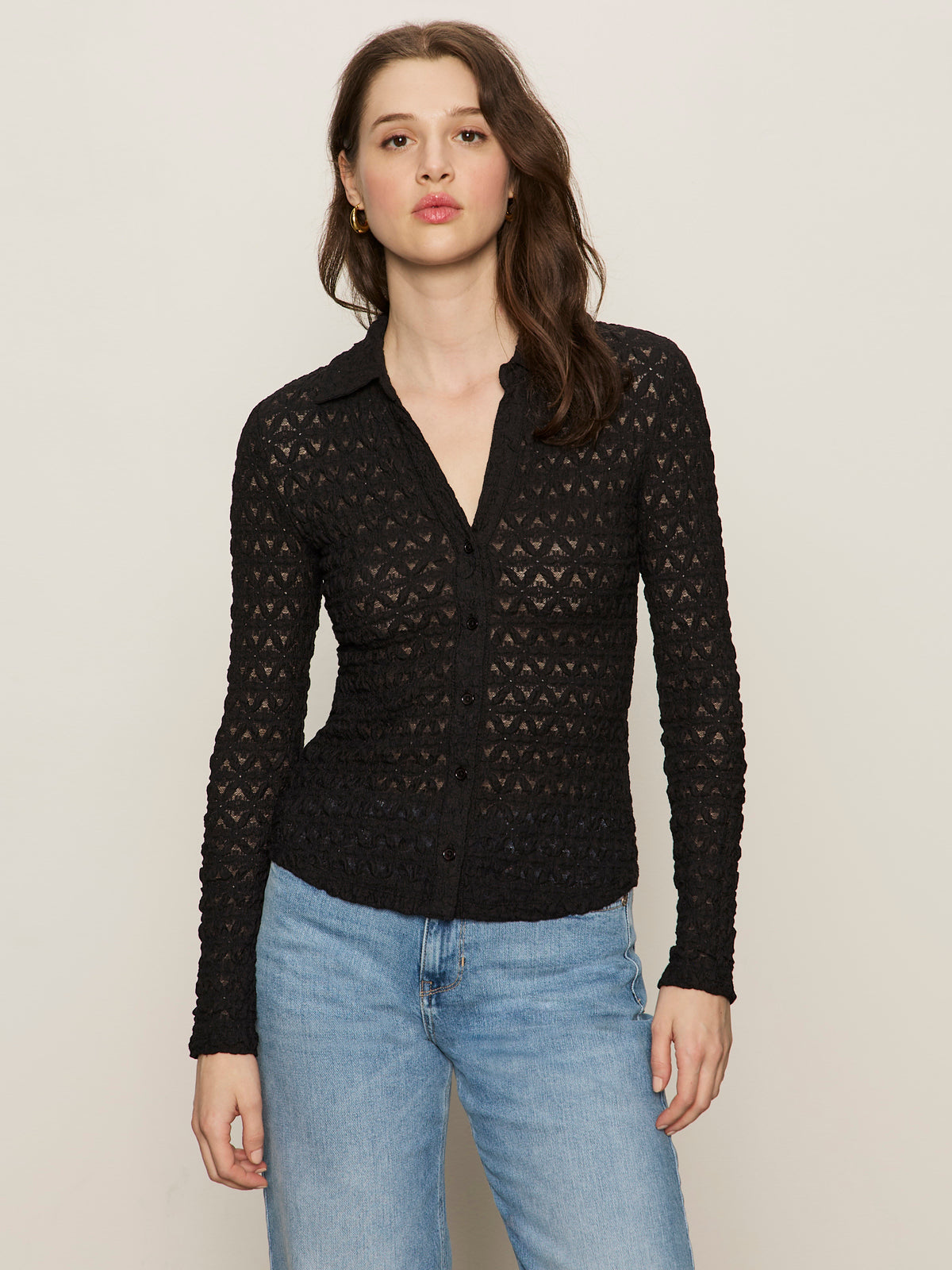 A woman with long brown hair and a neutral expression wears the Sanctuary Clothing dreamgirl lace button up black top and light blue jeans, standing against a plain background.