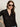 A woman with long brown hair, large sunglasses, and gold hoop earrings wears the Sanctuary Clothing dreamgirl lace button up black shirt, posing with one hand on her hip against a plain background.
