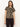 A woman with long brown hair and a neutral expression wears the Sanctuary Clothing double knit perfect tee winter leopard— a short-sleeved, beige t-shirt with black leopard spots — paired with dark brown pants, standing against a plain background.