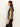 A woman stands in profile against a light background, wearing Sanctuary Clothing’s double knit perfect tee winter leopard—a short-sleeved, beige top with a black leopard print pattern—and dark pants. Her loose brown hair gives her a calm, relaxed look.