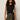 A woman with curly hair wears the Sanctuary Clothing side tie muscle tee in black, styled with olive green pants and a patterned belt, standing against a plain light background.
