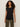 A woman with curly hair wears the Sanctuary Clothing side tie muscle tee in black, paired with olive green pants, standing against a plain light background.