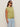 A woman wearing sunglasses, light blue jeans, and the Sanctuary Clothing knotted muscle tee bamboo (extended sizing) stands against a plain beige background.