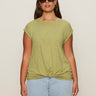 A woman wears dark sunglasses and the Sanctuary Clothing knotted muscle tee bamboo extended sizing in light olive green with light blue jeans, standing facing forward against a plain beige background.