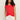 A woman with long curly hair wears the Sanctuary Clothing knotted muscle tee in cayenne and loose white pants, standing against a plain light background with her hands in her pockets.