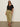 A woman wearing Sanctuary Clothing’s black notch neck tee (extended sizing), sunglasses, olive green drawstring pants, and black sandals stands against a plain light background on a gray floor.