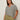 A woman with long brown hair models the Sanctuary Clothing notch neck tee light oat black stripe 3, paired with olive green drawstring pants, standing with one hand in her pocket against a plain light background.