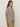 A woman with long brown hair and a neutral expression stands in profile against a plain background, wearing Sanctuary Clothing's notch neck tee light oat black stripe 3 and olive green pants.