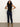 A woman with curly hair wears the Sanctuary Clothing sleeveless zip mock top in black, paired with dark blue jeans and tan suede boots, standing hands on hips against a plain light background.