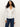 A woman with long curly hair wears the Sanctuary Clothing long sleeve textured top in chalk, styled with blue jeans, standing against a plain light background.