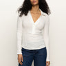 A woman with long curly hair wears the Sanctuary Clothing long sleeve textured top in chalk, styled with blue jeans, standing against a plain light background.