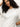 A woman with curly dark hair wears the Sanctuary Clothing shirred waist dolman tee in white, posing against a light background, one hand on her head, and looking confidently at the camera.
