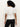A person with curly hair faces away from the camera, wearing Sanctuary Clothing’s white shirred waist dolman tee and black pants against a plain light background.
