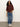 A woman with curly hair stands against a plain background, wearing the Sanctuary Clothing boxy raglan tee chicory, wide-leg blue jeans with rolled cuffs, and white sneakers. One hand is in her pocket as she gazes confidently at the camera.