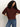 A person with long curly hair wears Sanctuary Clothing's boxy raglan tee in chicory and blue jeans, standing against a plain light background with hands on hips and head slightly tilted down.