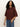 A woman with long curly hair wears the Sanctuary Clothing boxy raglan tee in chicory and blue jeans, standing against a plain light background while looking at the camera.