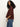 A woman with long curly hair models the Sanctuary Clothing boxy raglan tee in chicory, a loose-fitting maroon top with wide sleeves, paired with blue jeans and standing sideways against a plain white background.