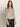 A woman with long wavy brown hair models the Sanctuary Clothing fitted mesh button down top mother leo, featuring a black and beige animal print, paired with high-waisted black leather pants against a plain background.
