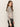 A woman with long wavy brown hair wears the Sanctuary Clothing fitted mesh button down top mother leo, an animal-print blouse, paired with black leather pants, standing sideways and looking at the camera against a plain background.