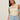 A woman with long brown hair wears the Sanctuary Clothing "waves of summer shell sweater macrame" in extended sizing, paired with light blue high-waisted jeans, standing against a plain light background with a neutral expression.