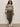 A woman with curly hair and a relaxed expression stands against a plain wall, wearing the Sanctuary Clothing fairisle sweater in light oat multi (extended sizing), olive green wide-leg cargo pants, white sneakers, and a light-colored belt.