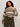 A woman with curly hair wears the Sanctuary Clothing fairisle sweater in light oat multi (extended sizing), tucked into high-waisted olive green pants with a belt, standing against a plain light background.