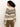A woman with curly dark hair stands in profile, wearing the Sanctuary Clothing fairisle crew neck sweater in light oat multi and brown pants, against a plain light background.