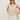 A woman stands confidently against a plain light background, hands in pockets, wearing sunglasses, white shorts, and the Sanctuary Clothing mesh stitch shell sweater macrame sleeveless cream knit top.
