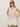 A woman stands confidently against a plain light background, hands in pockets, wearing sunglasses, white shorts, and the Sanctuary Clothing mesh stitch shell sweater macrame sleeveless cream knit top.