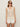 A woman with long, straight hair wears dark sunglasses, earrings, rings, and the Sanctuary Clothing mesh stitch shell sweater macrame—a sleeveless cream knit top—paired with white shorts against a plain background.