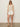 A woman wearing the Sanctuary Clothing mesh stitch shell sweater macrame stands against a plain light background, looking relaxed with sunglasses, white shorts, and beige slide sandals—one hand by her side.