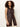 A woman with curly hair models the Sanctuary Clothing long openwork vest mesa, a sleeveless brown crochet button-up style, over light-colored pants against a plain light background.