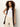 A woman with curly brown hair wears Sanctuary Clothing's long openwork vest mesa—a sleeveless, buttoned dark brown knit vest—over a white top and beige pants, standing against a plain light background with one hand on her hip.