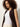 A woman with curly brown hair models the Sanctuary Clothing long openwork vest mesa over a sleeveless white top and cream pants, standing against a plain light background.