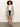 A woman with curly hair and a neutral expression poses against a plain background wearing the Sanctuary Clothing openwork beach cardi in chalk black stripe over a white t-shirt, denim shorts, a black belt, and black sandals.