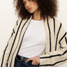 A woman with curly hair wears the Sanctuary Clothing openwork beach cardi in chalk black stripe over a white t-shirt and denim jeans, standing against a plain light background.