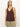 A woman with straight, light brown hair models the Sanctuary Clothing v neck knitwear tank mesa in dark brown, paired with light green pants. She stands against a plain background, gazing slightly to the side with a neutral expression.