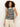 A woman with curly hair wears Sanctuary Clothing’s modern sweater shell in black macrame and light beige pants, standing against a light background with one hand in her pocket.