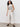 A person with curly hair wears the Sanctuary Clothing ribbed funnel neck top in light oat black 3, paired with white wide-leg pants and black woven flats, standing against a plain light-colored wall.