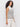 A woman with long curly hair models the Sanctuary Clothing ribbed funnel neck top light oat black 3, a sleeveless high-neck cream top with black stripes, paired with cream pants against a plain white background.