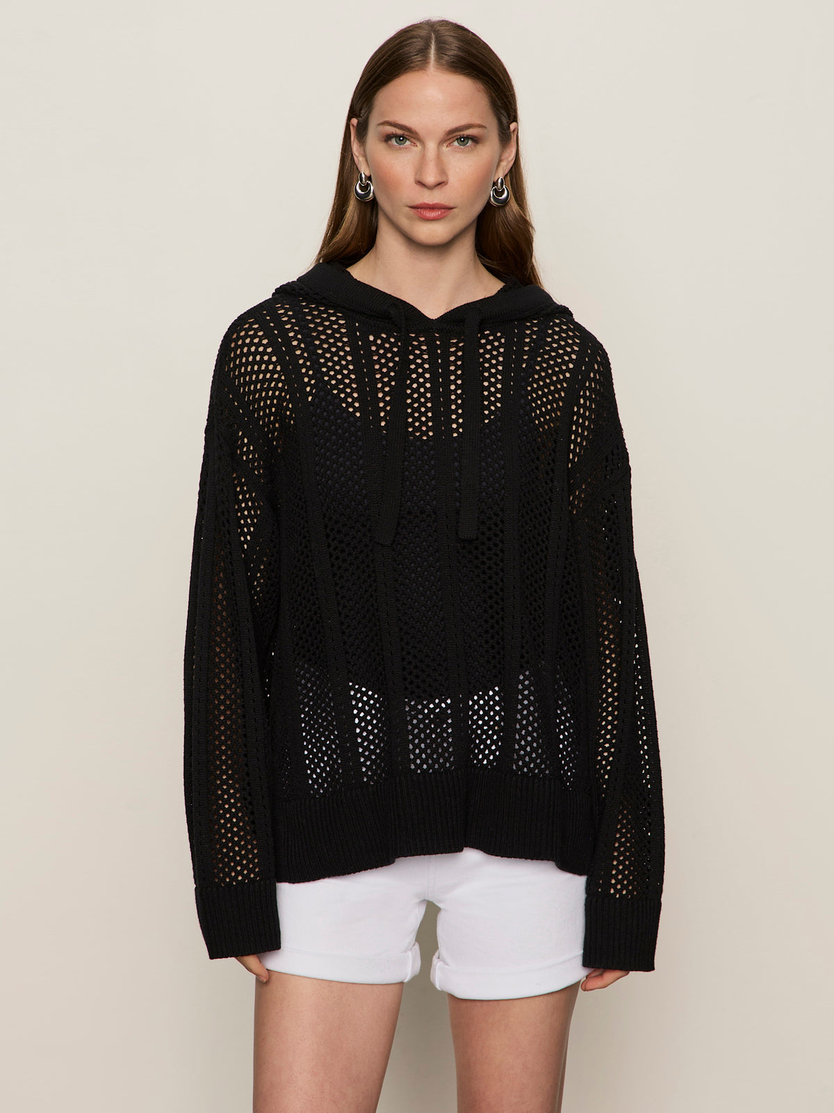 A woman with straight brown hair wears the Sanctuary Clothing beach hoodie in black over a black top and white shorts, standing against a plain background and looking directly at the camera with a neutral expression.