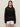 A woman with straight brown hair wears the Sanctuary Clothing beach hoodie in black over a black top and white shorts, standing against a plain background and looking directly at the camera with a neutral expression.