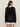 A woman with long brown hair wears the Sanctuary Clothing beach hoodie black, a loosely knit mesh sweater, over white shorts. The see-through hoodie features a relaxed fit and is styled against a plain beige background.