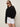 A woman models the Sanctuary Clothing beach hoodie black, paired with white shorts, sunglasses, and hoop earrings, standing against a plain light background with one hand in her pocket.