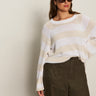 A woman in Sanctuary Clothing's textured raglan crew in white light oat stripe (extended sizing) and high-waisted olive green pants stands against a plain light-colored background.