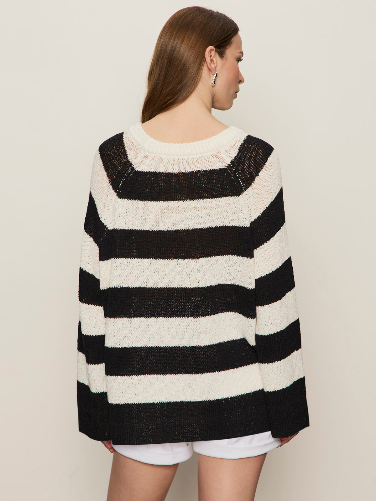 A woman with long brown hair, seen from the back, wears Sanctuary Clothing's textured raglan crew chalk black stripe 6 sweater with white shorts against a plain light background.