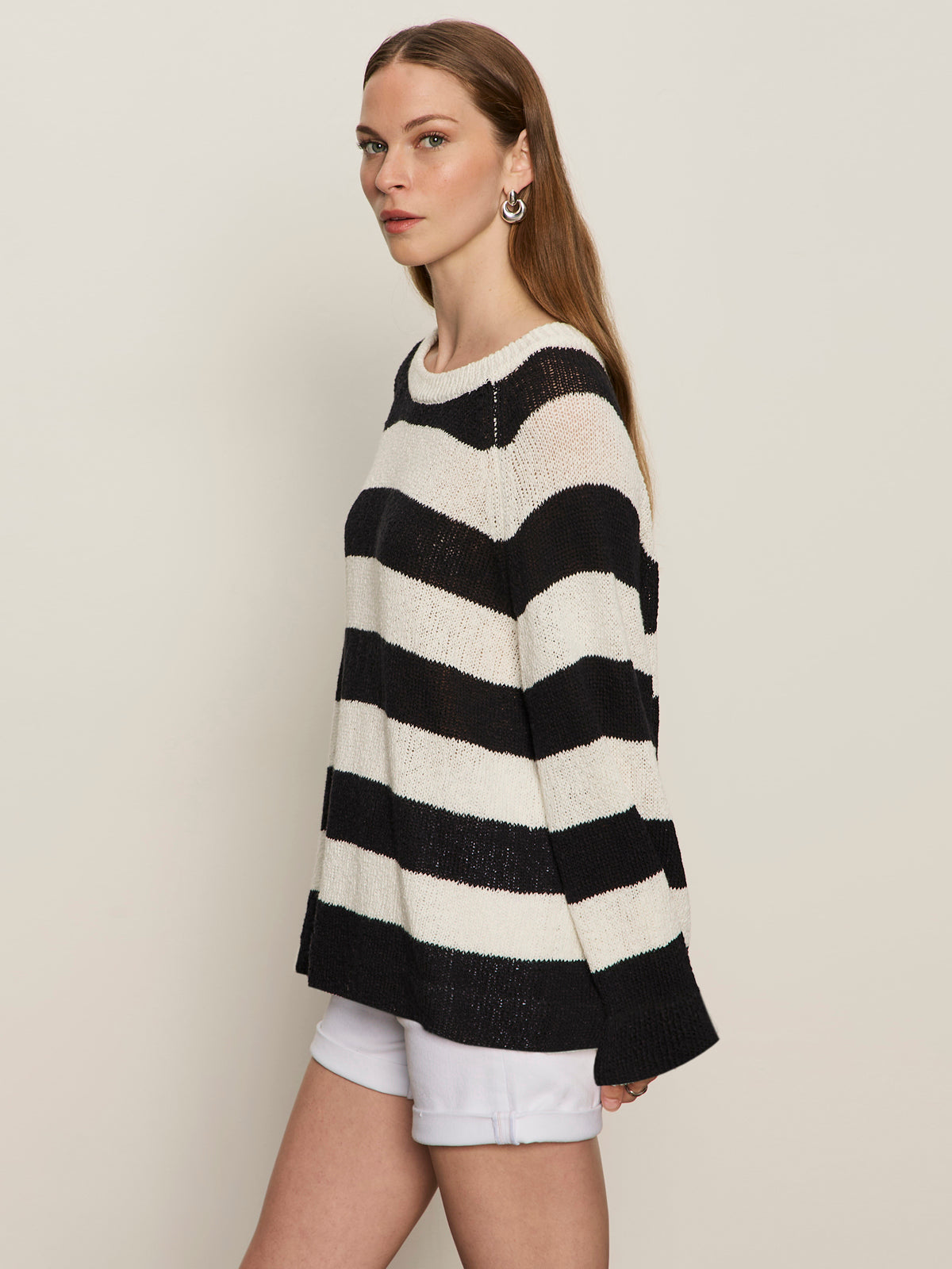 A woman with straight brown hair and hoop earrings stands sideways against a light background, wearing Sanctuary Clothing's textured raglan crew chalk black stripe sweater (size 6) and white shorts.