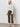 A woman stands against a white wall wearing the Sanctuary Clothing textured raglan crew in white light oat stripe. She smiles softly with one hand by her side, pairing the sweater with olive cropped pants and light woven slip-on shoes.