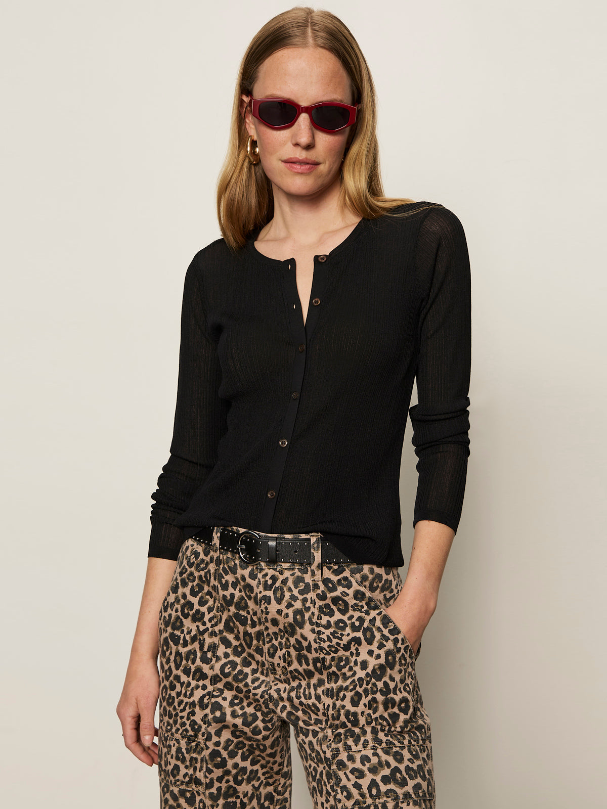 A woman wears the Sanctuary Clothing lightweight ribbed cardi in black, paired with leopard print pants, a black belt, red sunglasses, and gold hoop earrings against a plain light background.