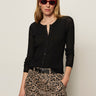A woman wears the Sanctuary Clothing lightweight ribbed cardi in black, paired with leopard print pants, a black belt, red sunglasses, and gold hoop earrings against a plain light background.